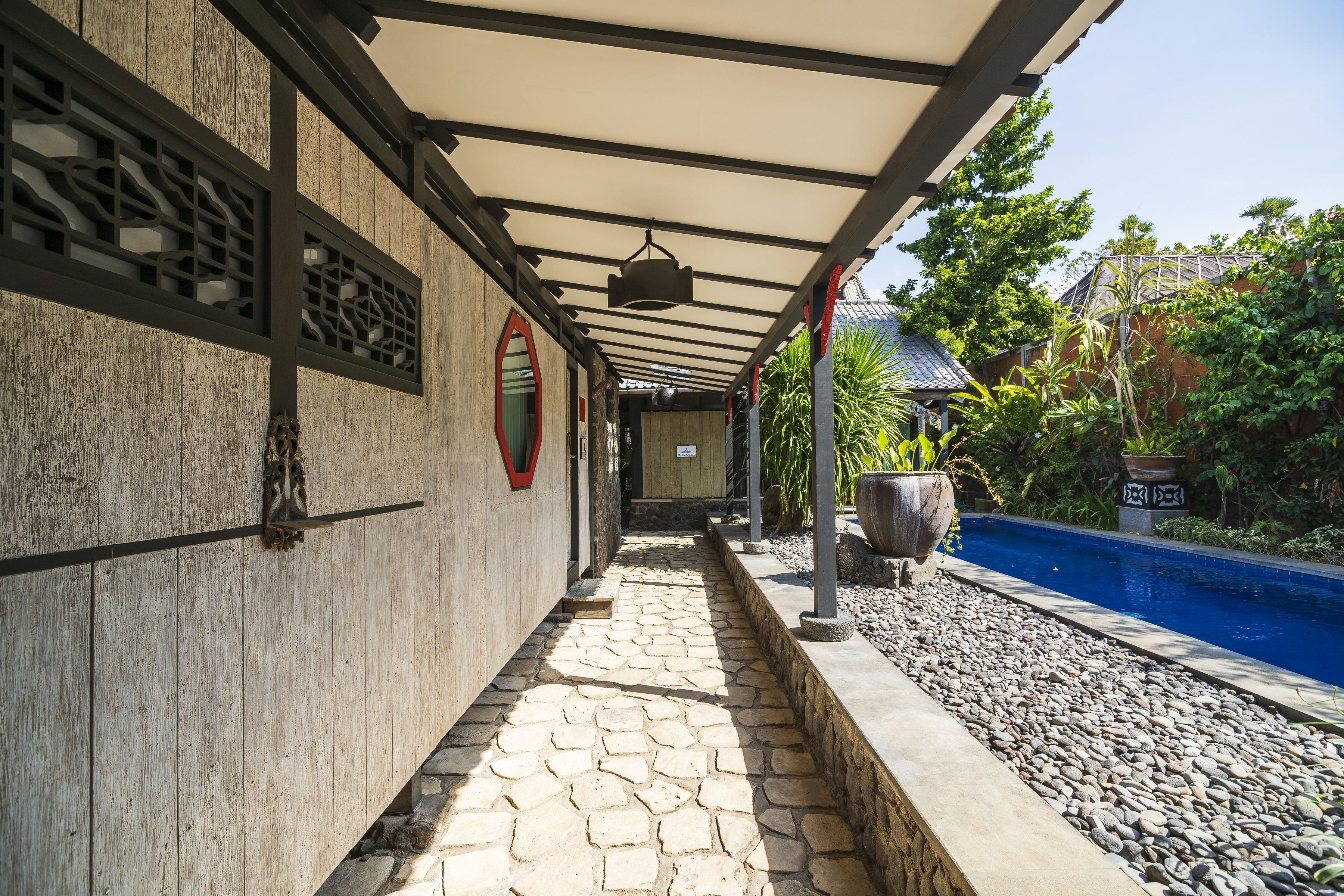 A covered walkway with stone flooring, a pool, and a building with traditional architectural elements.