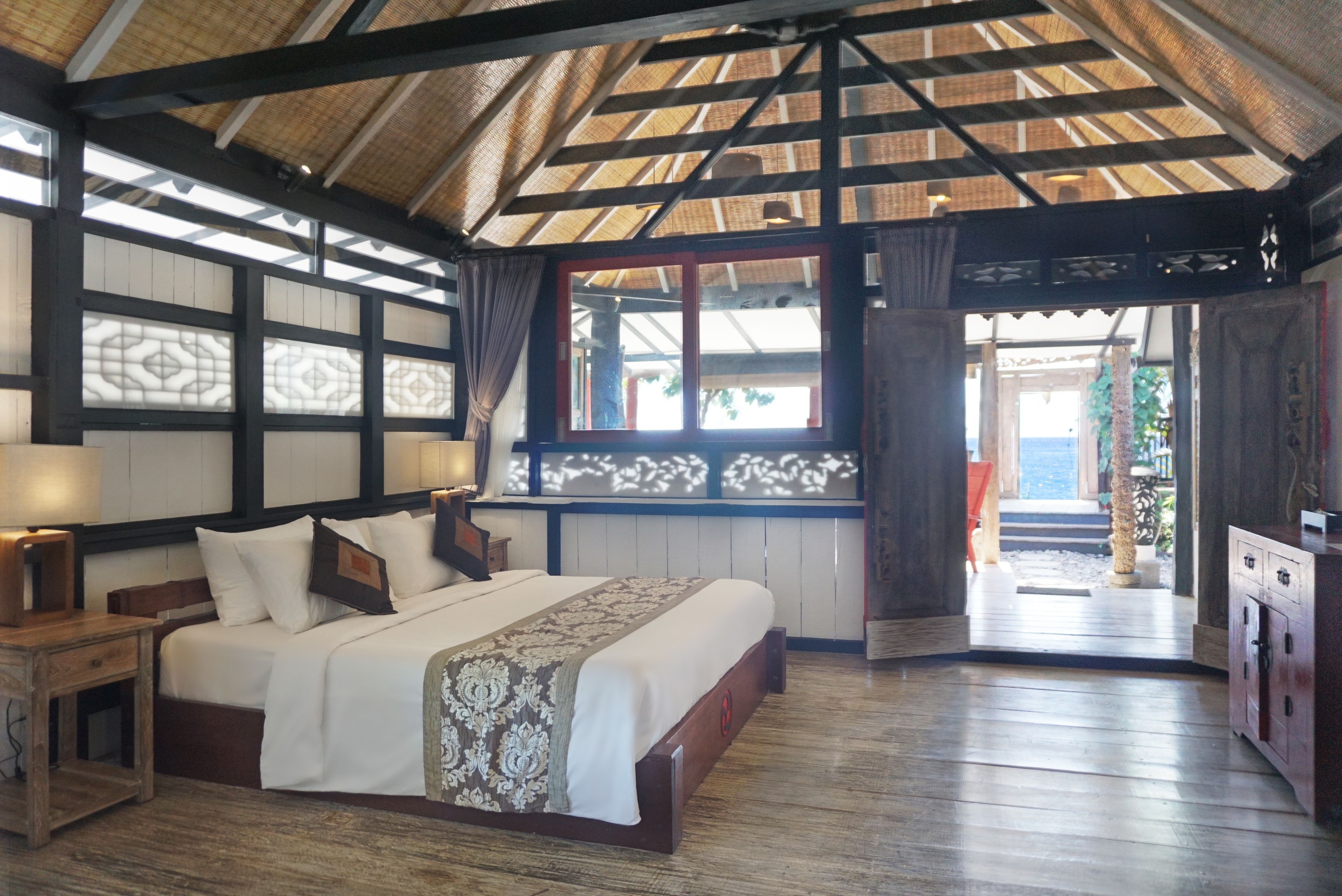 A traditional-style bedroom with a large bed, wooden headboard, and a thatched roof.
