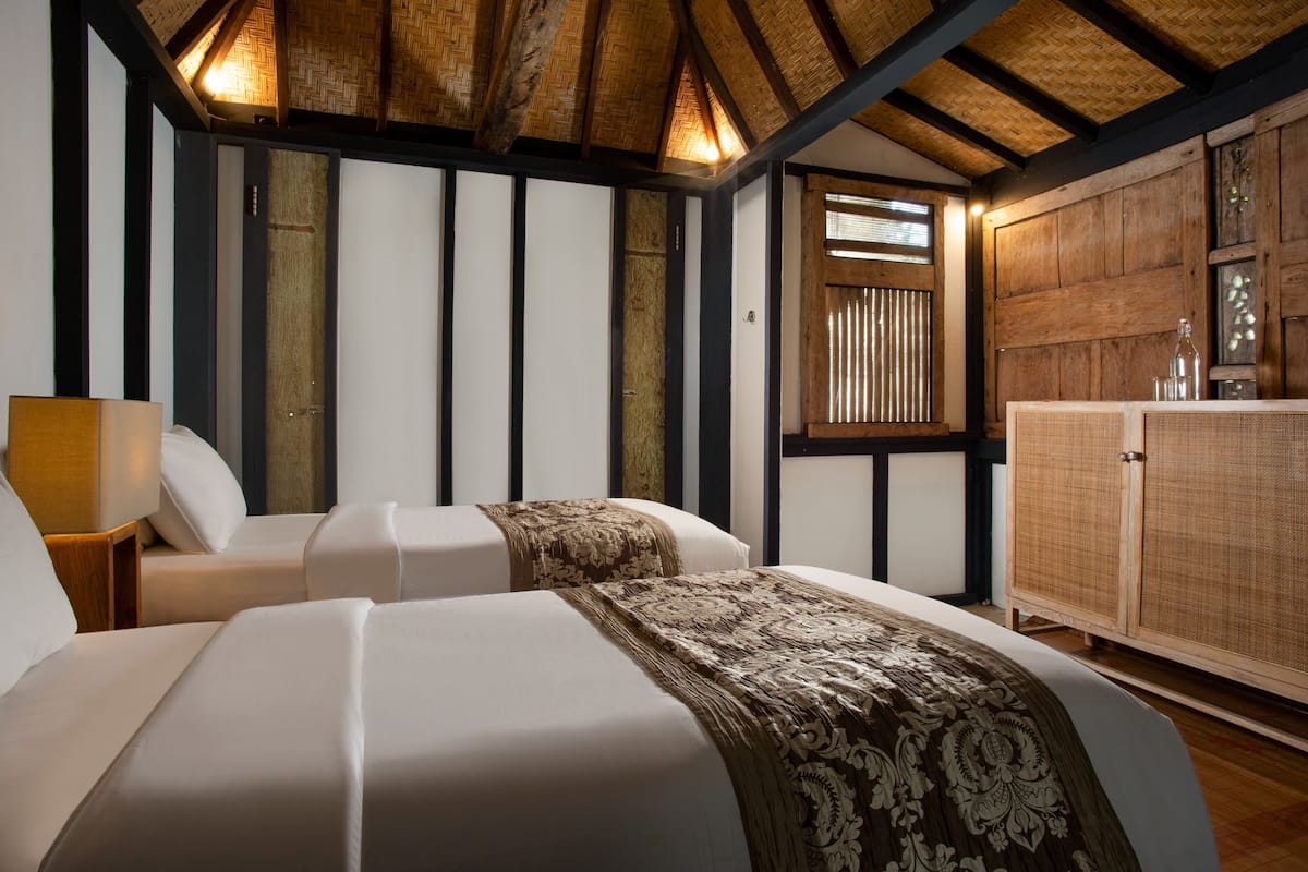 A room with two beds, a wooden cabinet, and a large window with blinds.