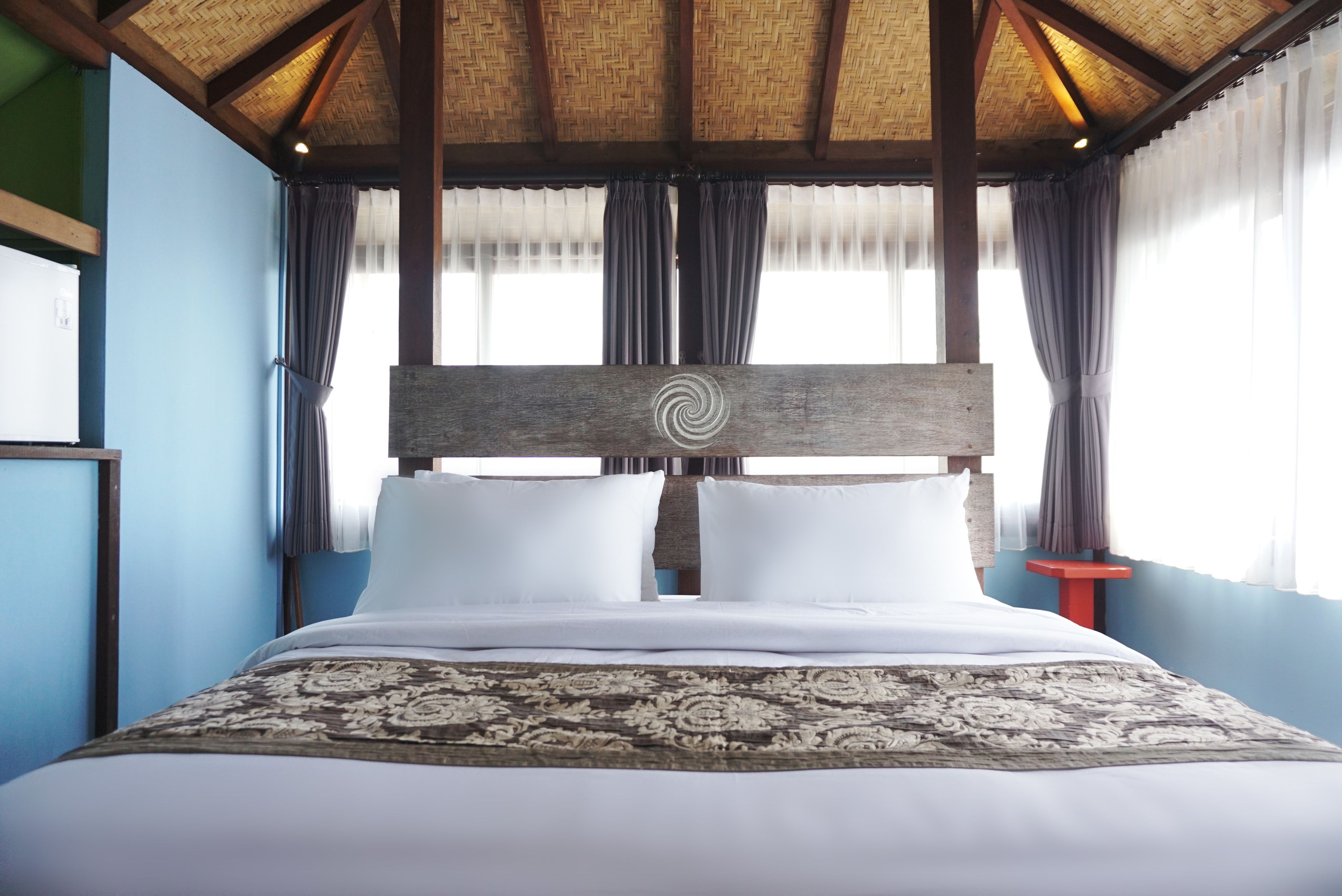 Ein großes Bett mit Holz-Kopfteil und einem gemusterten Überwurf in einem Zimmer mit blauen Wänden und einem Reetdach.