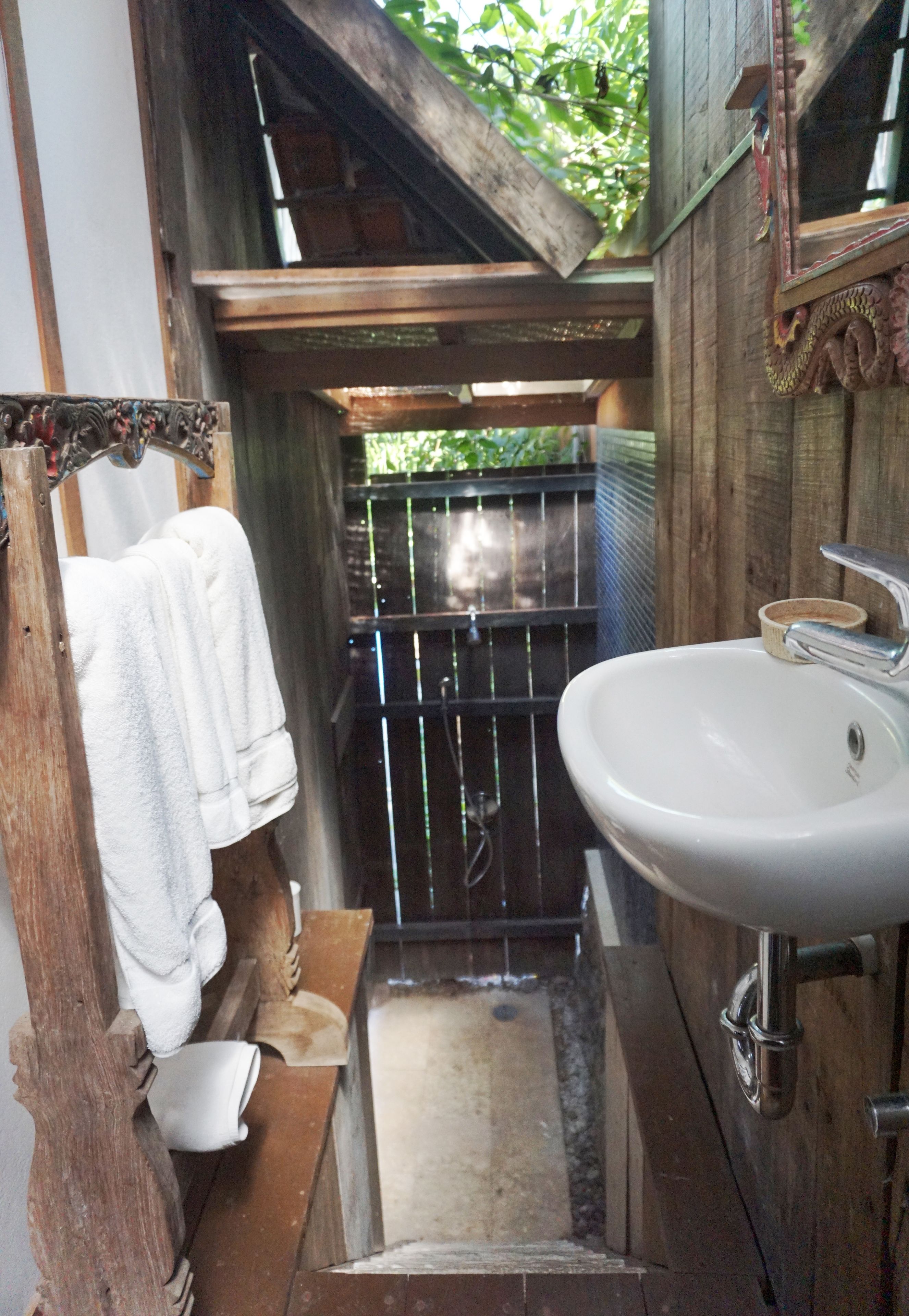 A narrow bathroom with a wooden door, a white sink, and a towel hanging on a wooden rack.