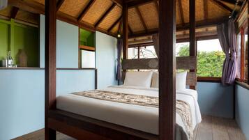A room with a bed, wooden beams, a window with curtains, and a view of greenery outside.