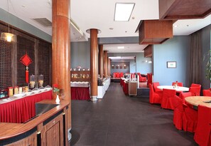 Un restaurant avec des nappes rouges, des piliers en bois et un long comptoir où sont présentés différents plats.