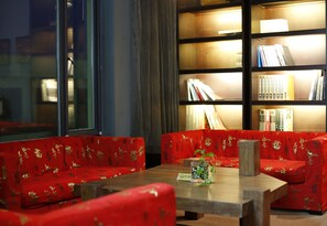Une pièce avec des canapés recouverts d’un tissu rouge, une table en bois et une bibliothèque remplie de livres.