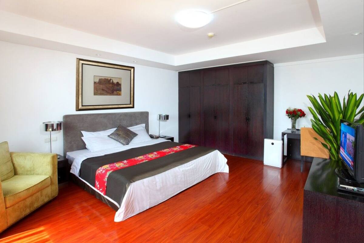 Um quarto moderno com uma cama grande, uma mesa de cabeceira, uma cadeira, um guarda-roupa e uma televisão.