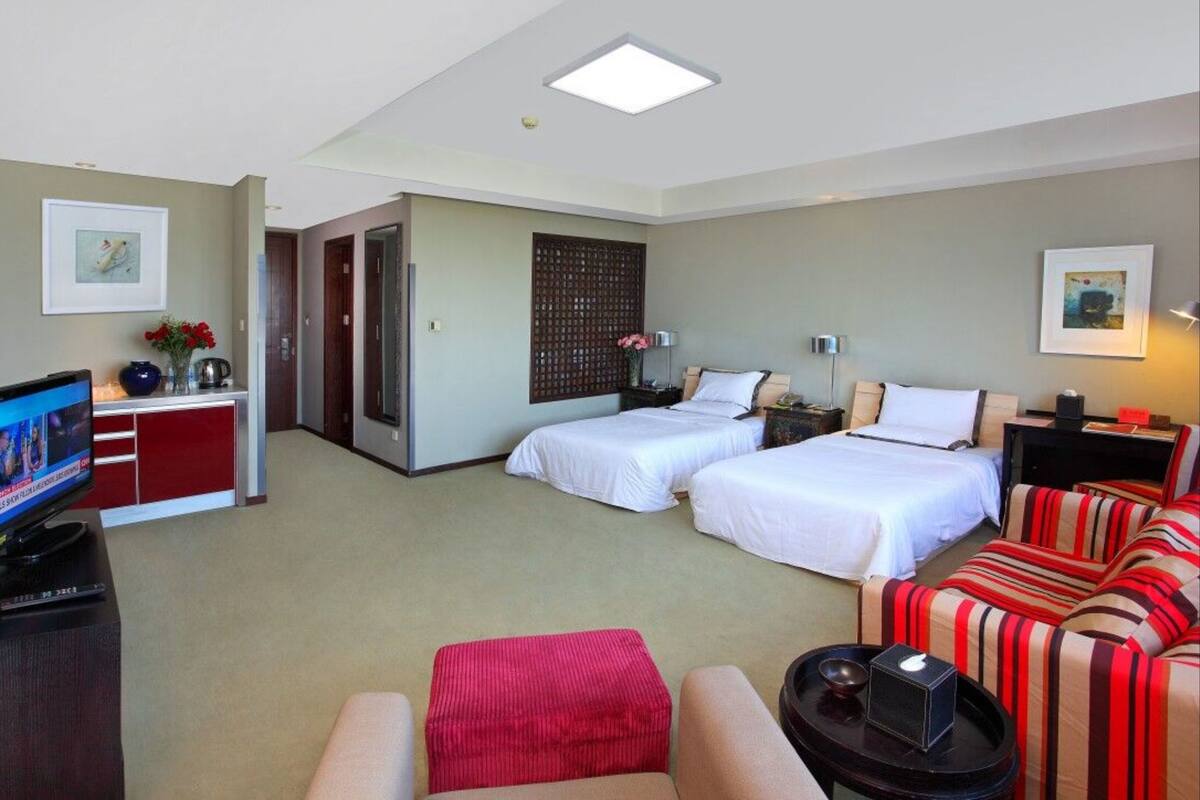 Quarto de hotel com duas camas, um sofá, uma televisão e uma escrivaninha com computador.