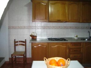 A kitchen with wooden cabinets, a tiled backsplash, a sink, and a table with a basket of oranges. - Country Cottage / Gite - Pozoblanco (Pozoblanco)