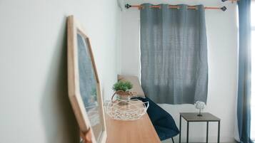 A minimalist room with a wooden desk, a small side table, a chair, a large window with curtains, and a wall-mounted mirror.