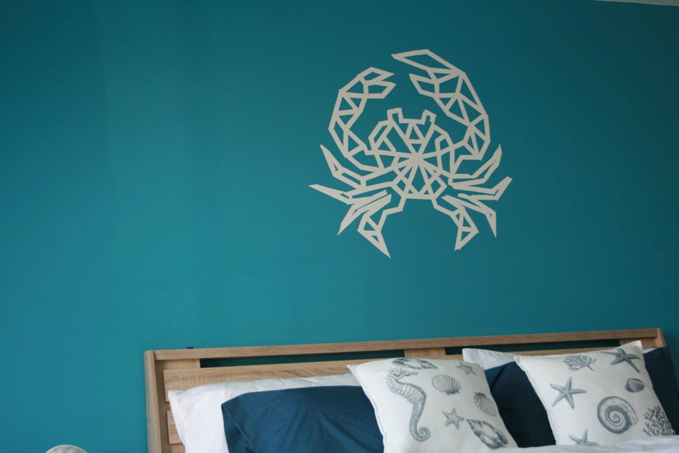 A room with teal walls, a wooden bed frame, and a geometric wall decoration.