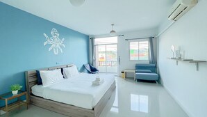Een moderne hotelkamer met een groot bed, een blauwe accentmuur, een balkon met uitzicht en een klein zithoekje.