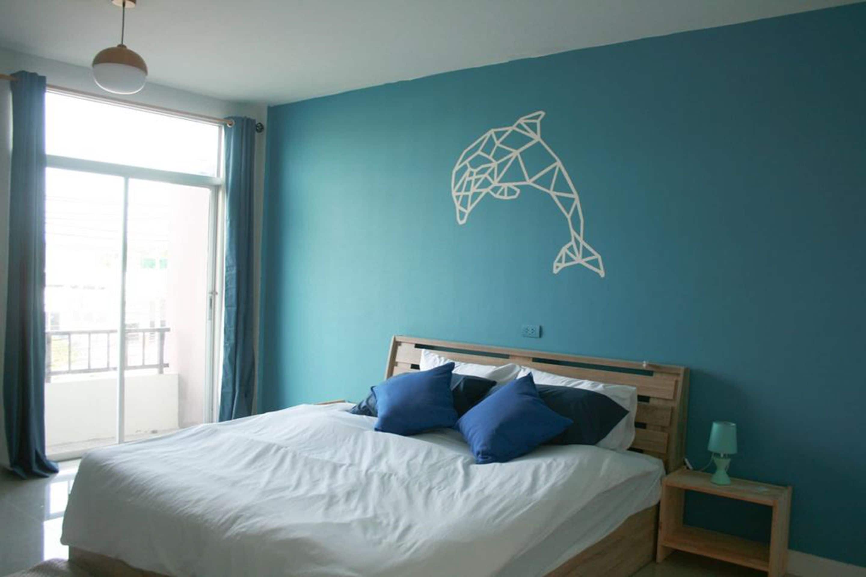 A bedroom with a bed, blue curtains, a wall art of a dolphin, and a nightstand with a lamp.