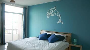 A bedroom with a bed, blue curtains, a wall art of a dolphin, and a nightstand with a lamp.