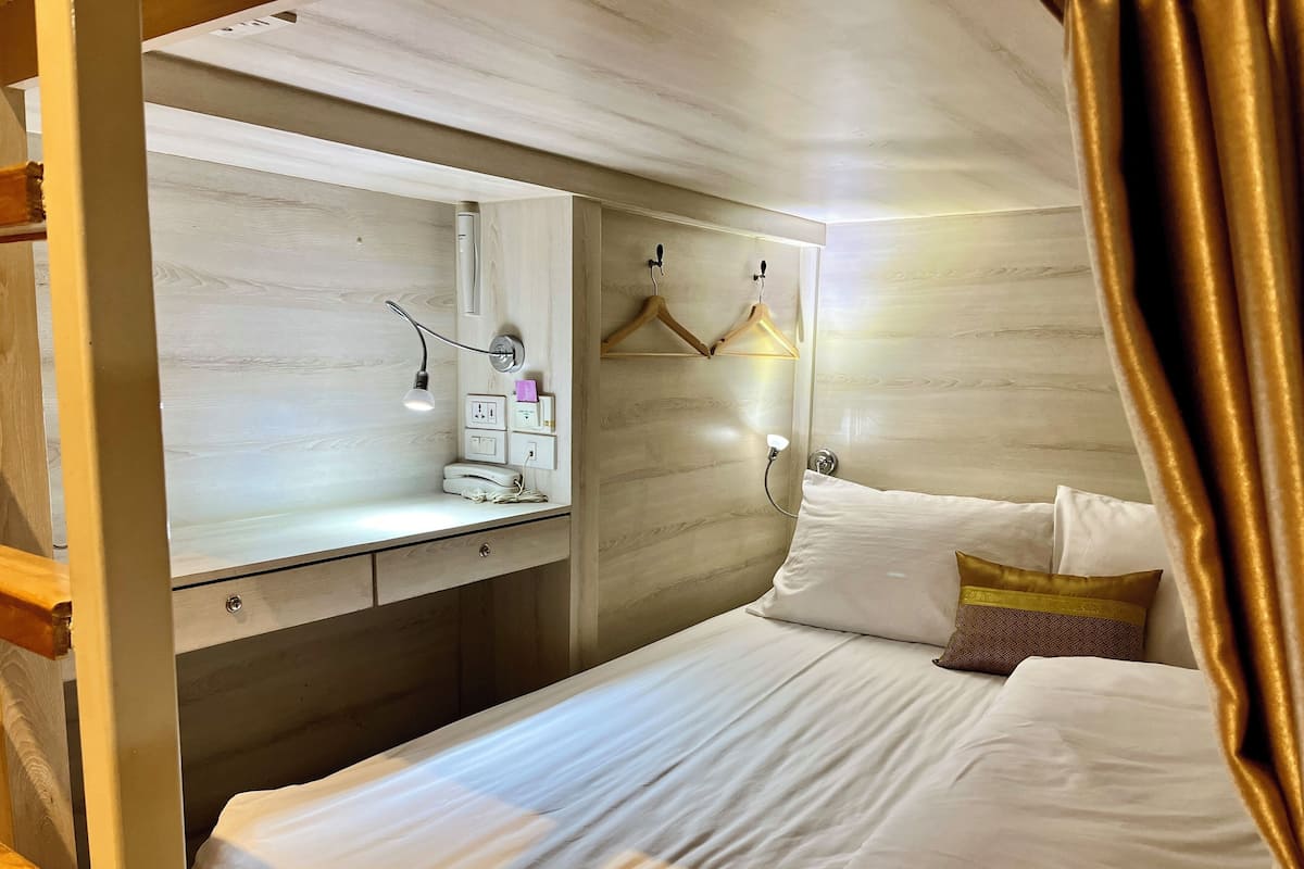 A bedroom with a bed, a bedside table, a mirror, and a wall-mounted light fixture.