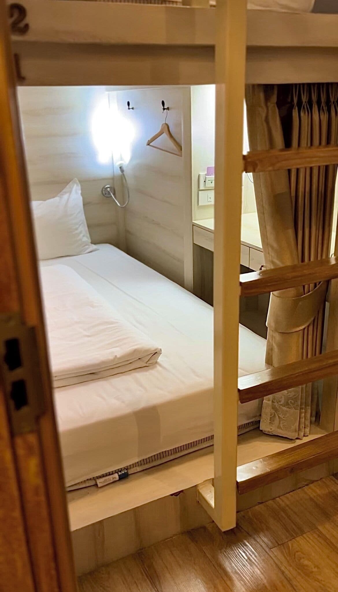 A bunk bed with a white mattress, a wooden ladder, and a small bedside table with a lamp.
