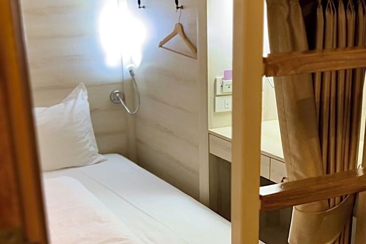A bunk bed with a white mattress, a wooden ladder, and a small bedside table with a lamp.