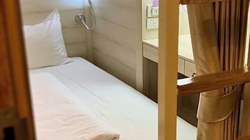 A bunk bed with a white mattress, a wooden ladder, and a small bedside table with a lamp.
