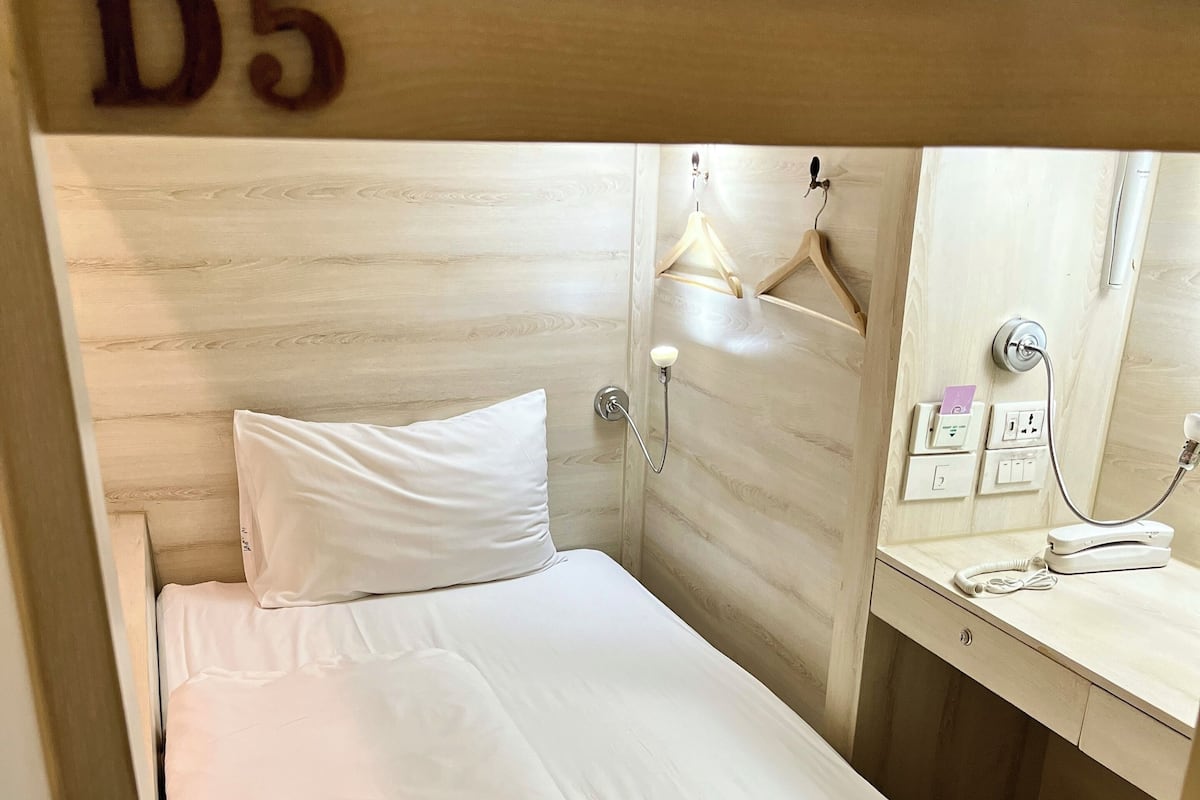 A single bed with white bedding in a room with wooden paneling and a number 'D5' on the wall.