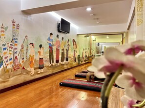 Una habitación con un mural que representa figuras tradicionales, suelo de madera y un televisor montado en la pared.