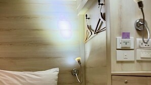Ein kleines Zimmer mit einem Einzelbett, einem Holzkopfstück, einem Nachttisch mit Lampe und einem Wandhandtuchhalter.