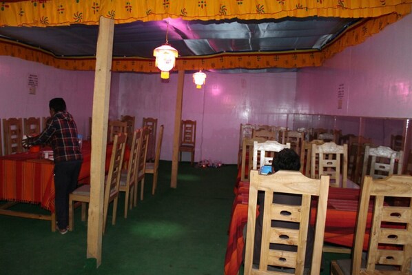 A room with wooden chairs and tables, a person at a table, and hanging lanterns. - Auspicious Camps and Cottages (Leh)