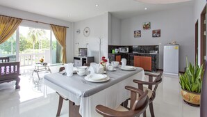 Un comedor con una mesa dispuesta para cuatro personas, una cocina al fondo y un balcón con cortinas.