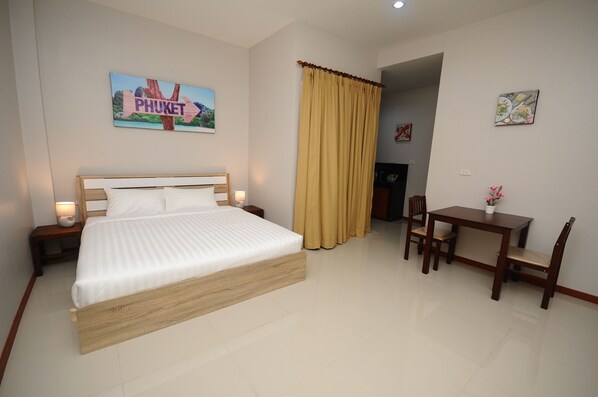 A hotel room with a large bed, a desk with two chairs, a small table with a potted plant, and a painting on the wall.