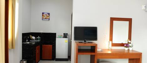 A compact room with a kitchenette, a wooden desk with a TV, and a mirror.