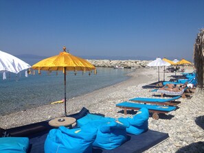 A beach with sun loungers and umbrellas, a rocky shoreline, and calm water.