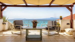 Eine Terrasse mit Tisch und zwei Stühlen, mit Blick auf ein Gewässer und Berge in der Ferne.