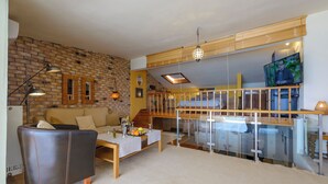 Ein großzügiger Wohnbereich mit Backsteinwand, einer Couch, einem Couchtisch mit Früchten und einem Fernseher auf einem Holzbodenständer.
