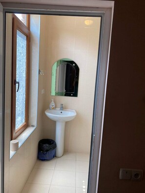 Een badkamer met een witte wastafel, een spiegel en een raam.