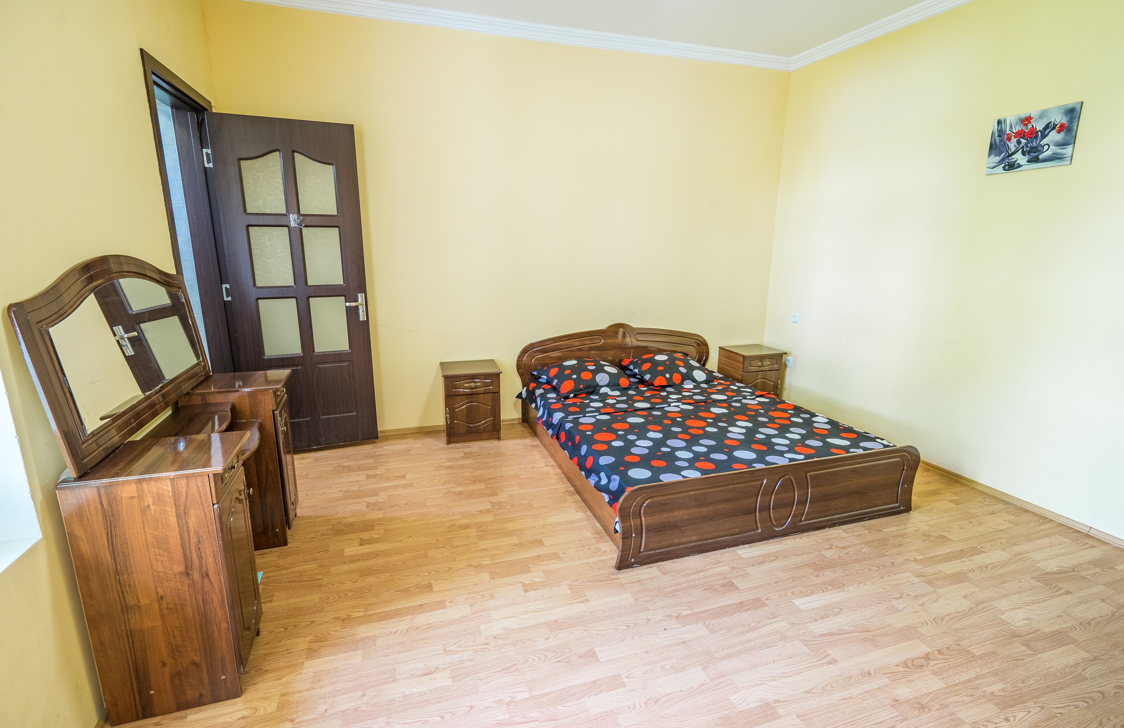 Un dormitorio con una cama de madera, un tocador, un espejo y una puerta.