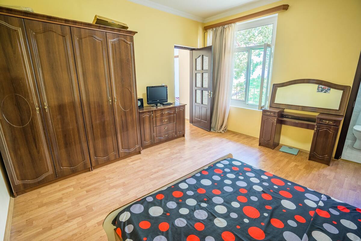 A bedroom with a bed, wardrobe, desk, and a window with curtains.