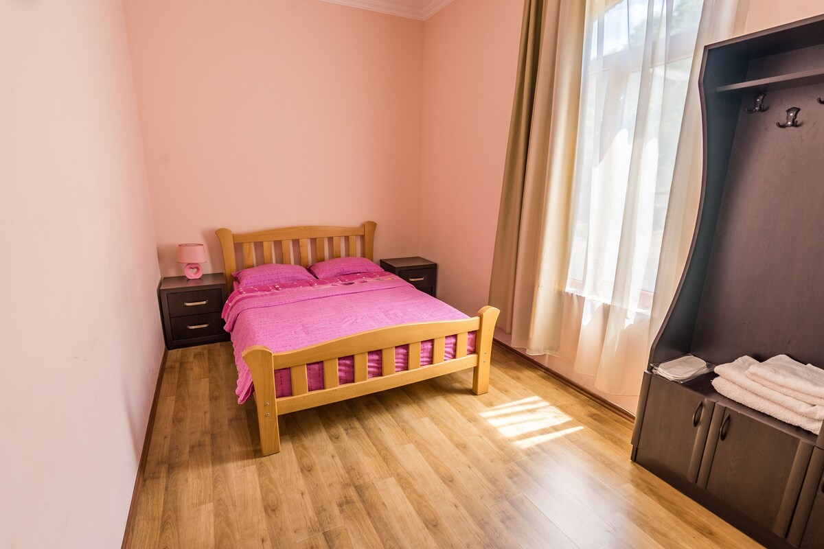 Een slaapkamer met een houten bed, een nachtkastje met een lamp, een kledingkast en een raam met gordijnen.