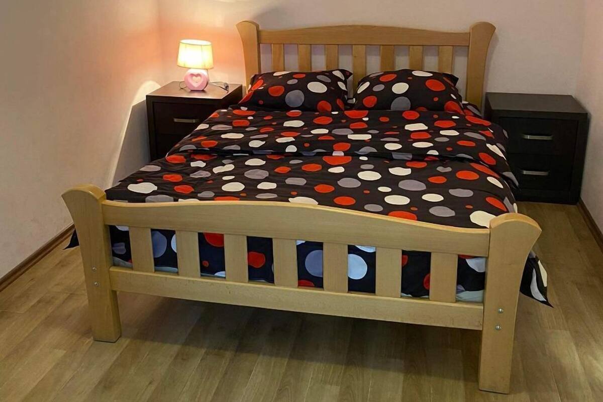 A single bed with a wooden frame and a polka dot bedspread in a room with a wooden floor and a nightstand with a lamp.