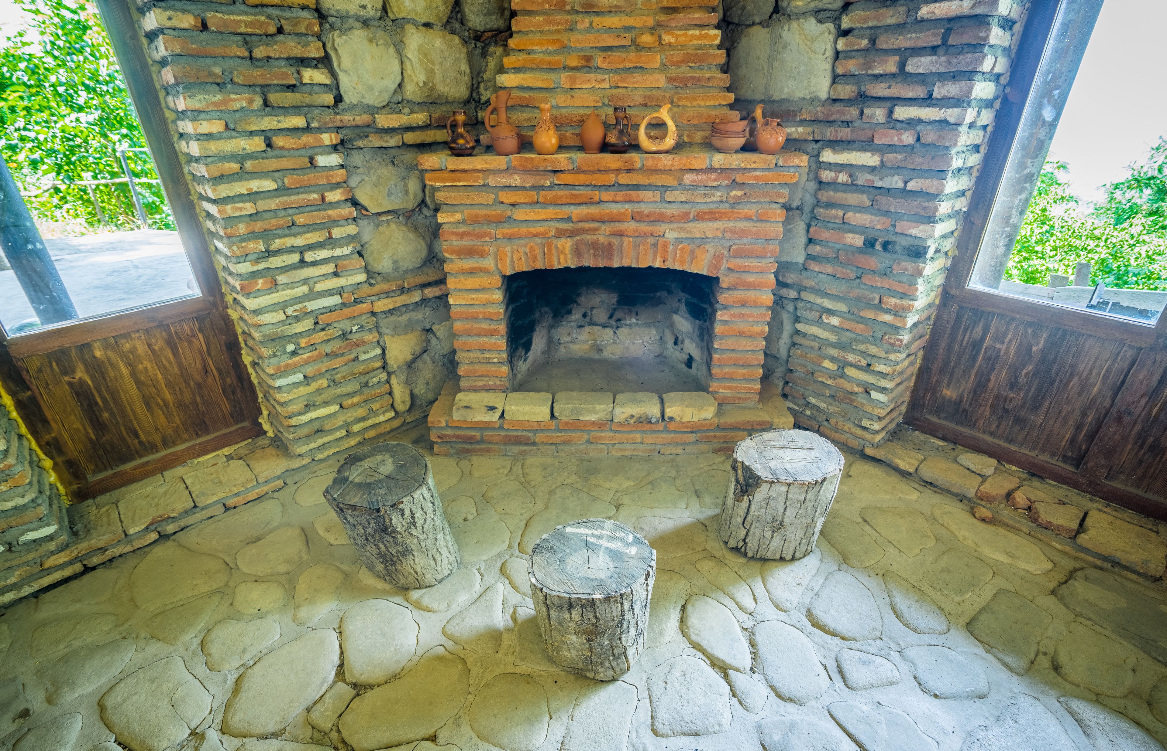 A rustic brick fireplace with pottery and a stone floor.