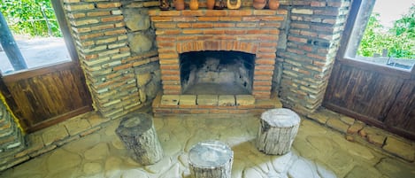 A rustic brick fireplace with pottery and a stone floor.