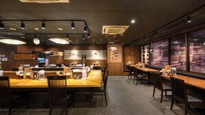 A restaurant interior with multiple dining tables, chairs, ceiling lights, and a menu display. - JR WEST GROUP VIA INN SHIMONOSEKI (Shimonoseki)
