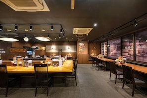 A restaurant interior with multiple dining tables, chairs, ceiling lights, and a menu display.