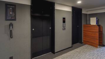 A hotel lobby with a floor plan sign, an elevator, a reception desk, and a phone on the wall.
