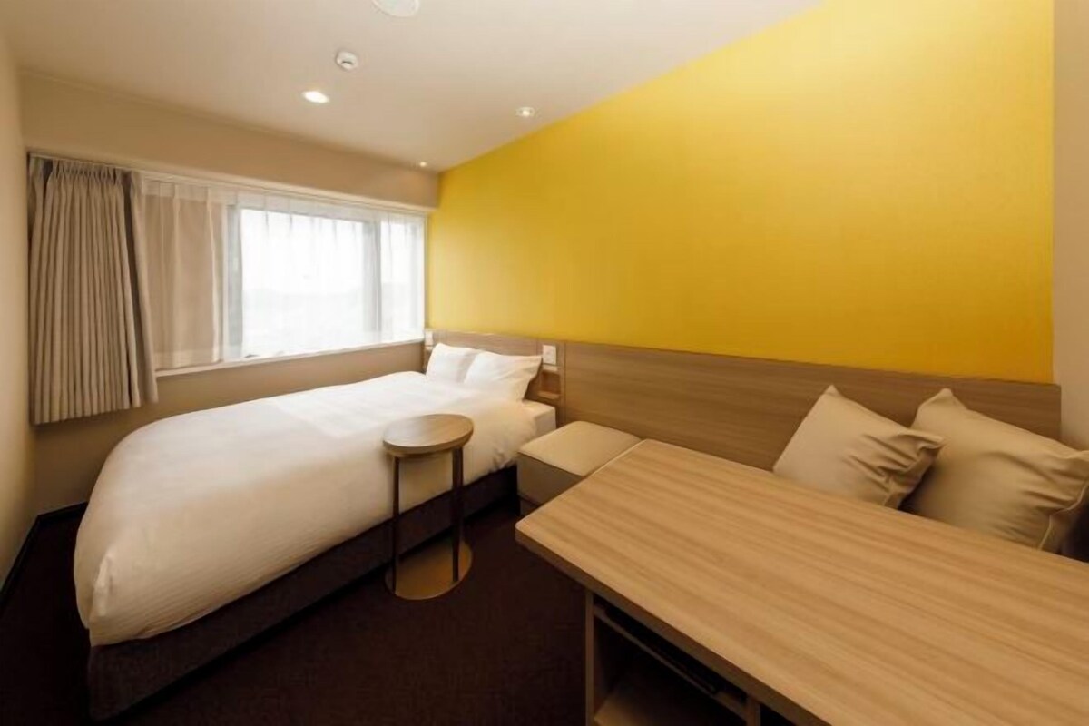A hotel room with a large bed, a bedside table, a small round table, and a wooden bench.