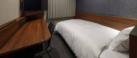 A hotel room with a bed, a desk, a television, and a window with curtains.