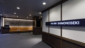 A hotel lobby with a reception desk, a seating area with a sofa and a small table, and a wall with a sign that reads "VIA INN SHIMONOSEKI". - JR WEST GROUP VIA INN SHIMONOSEKI (Shimonoseki)