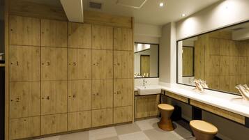 A modern bathroom with wooden lockers, a sink, and two toilets.