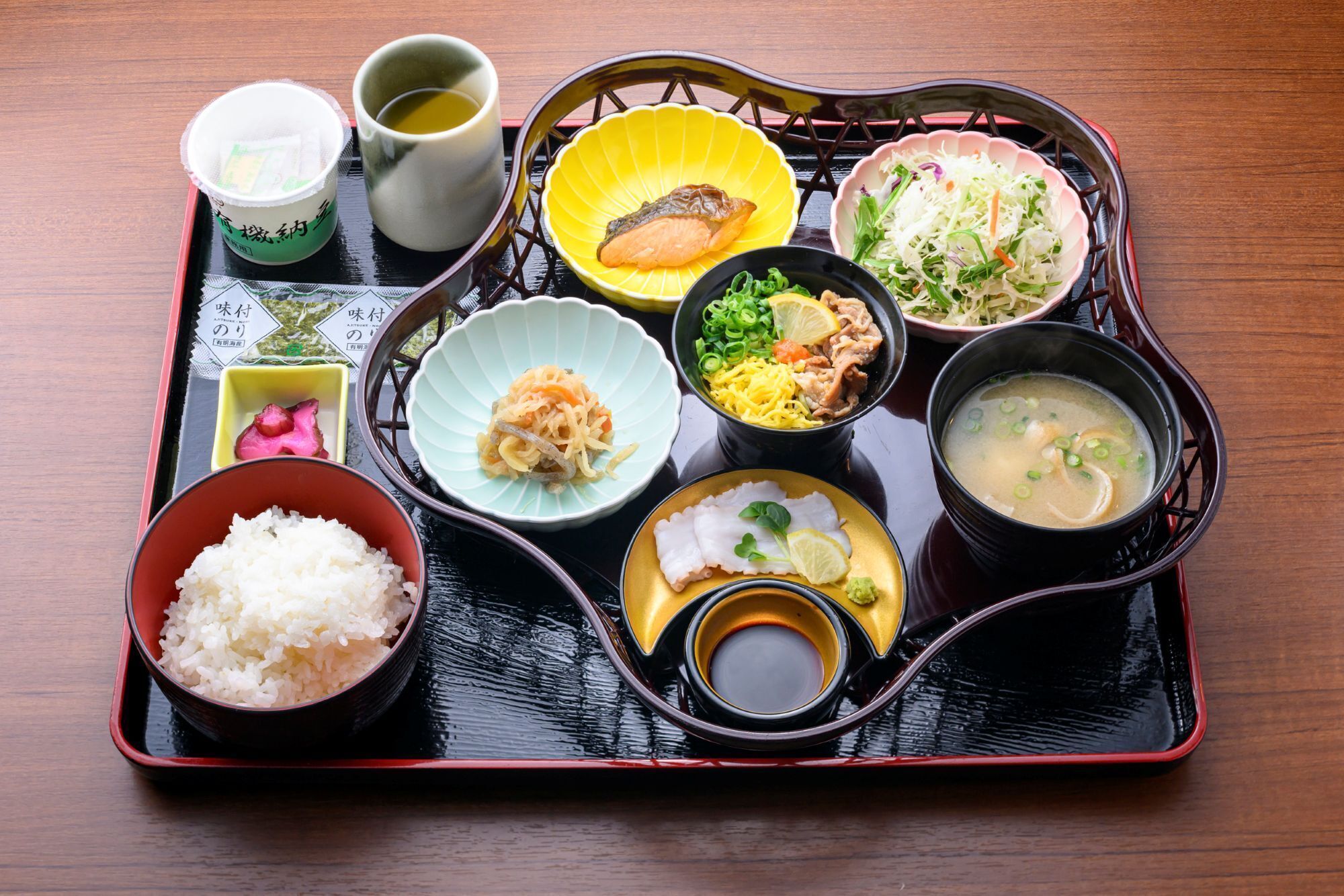 A traditional Japanese meal set on a black tray with various dishes including rice, soup, and vegetables.