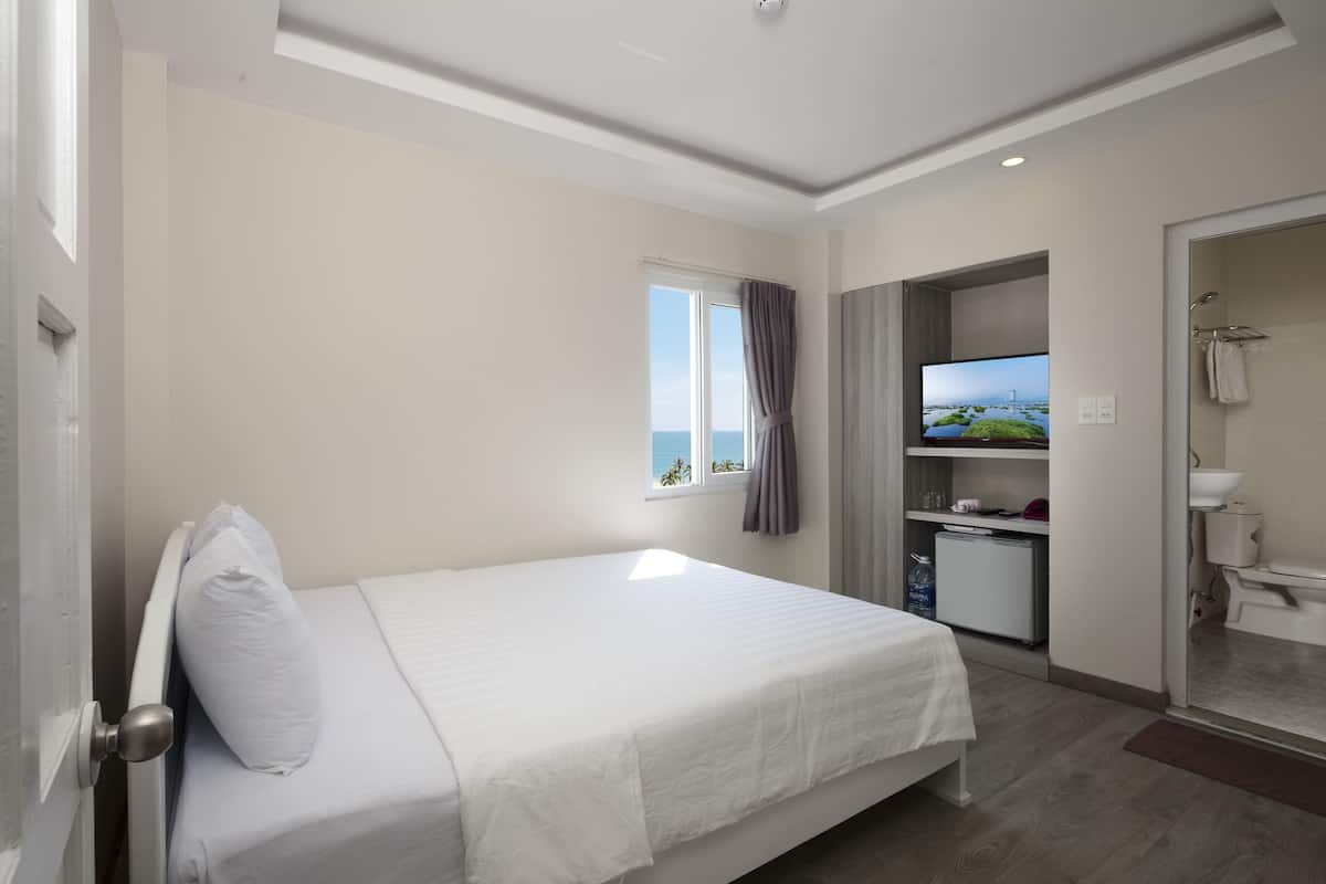 Quarto de hotel com cama, televisão, pequena cozinha e banheiro.