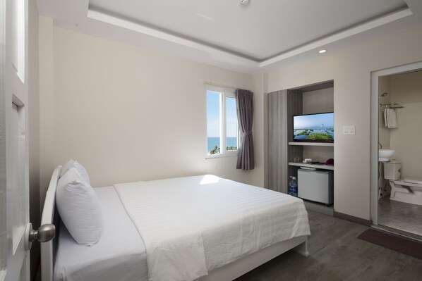 A hotel room with a bed, a television, a small kitchenette, and a bathroom.