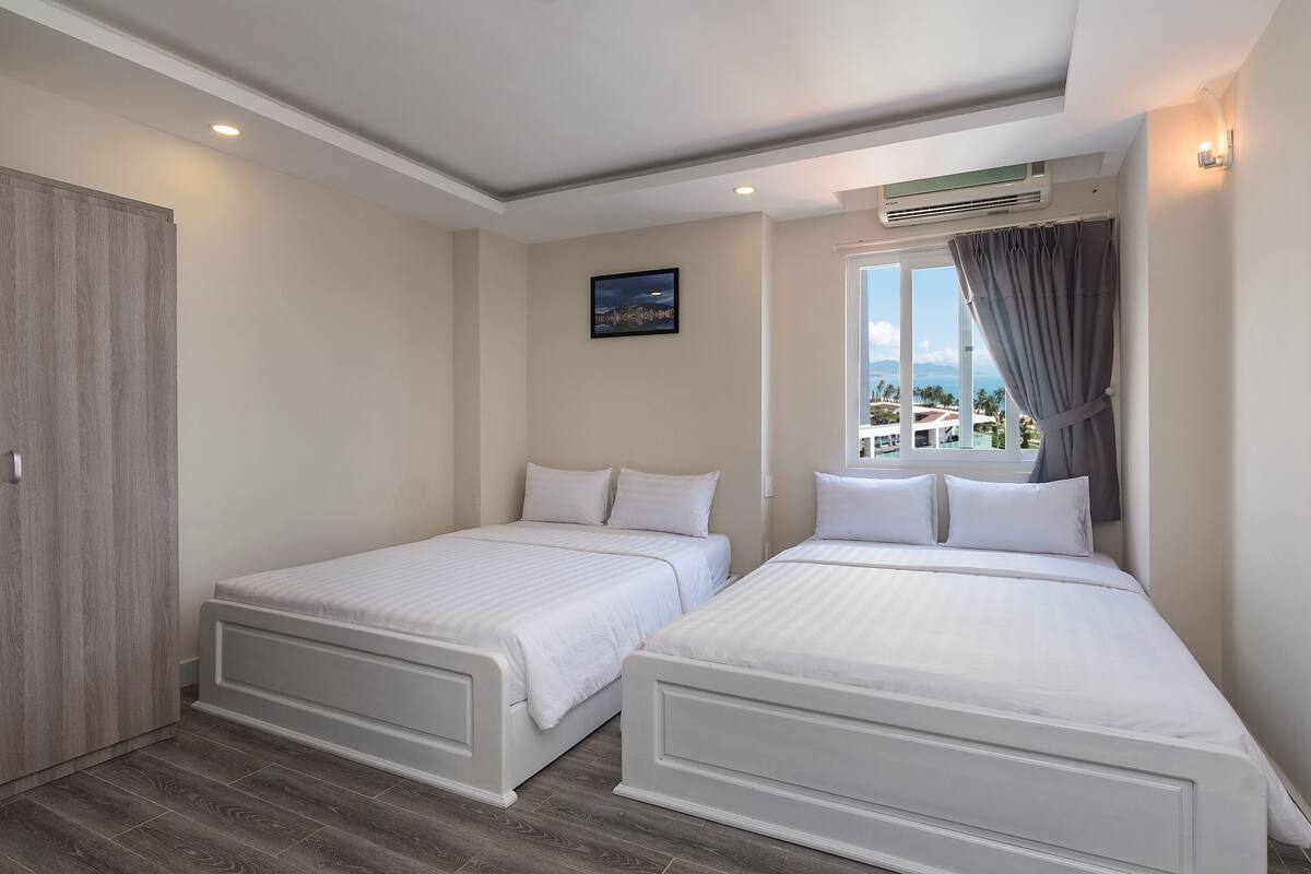 Quarto de hotel com duas camas de solteiro, um guarda-roupa, uma janela com cortinas e vista para a cidade.