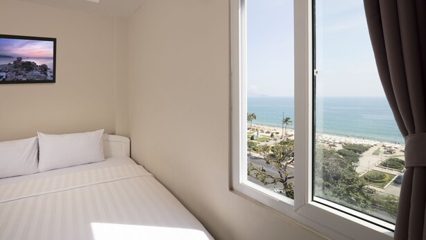 A bedroom with a large window offering a view of a beach and ocean. - Zen Hotel (Nha Trang)