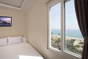A bedroom with a large window offering a view of a beach and ocean. - Zen Hotel (Nha Trang)